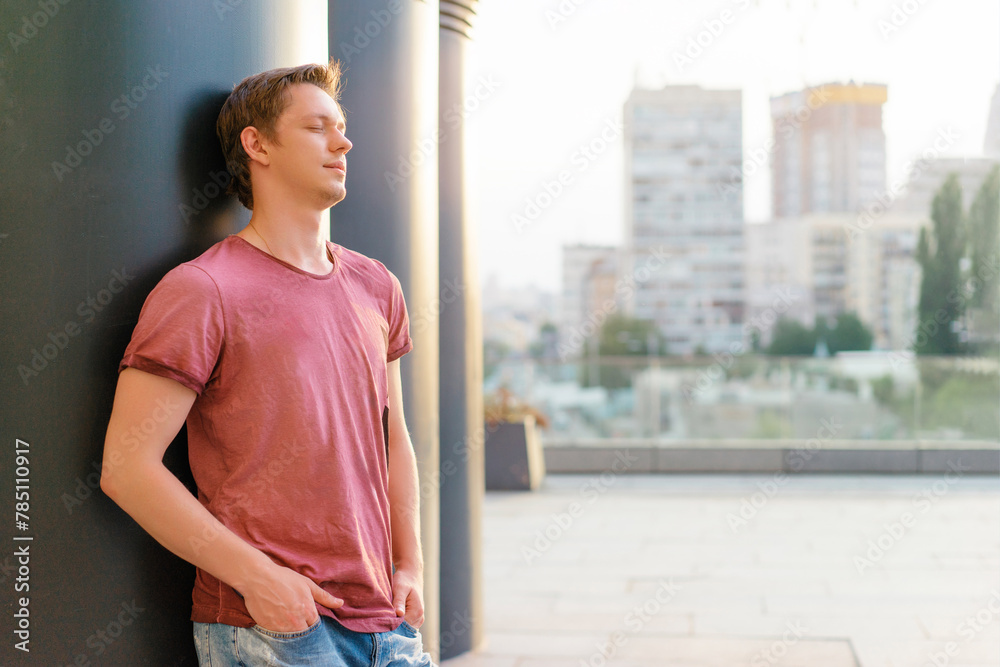 Handsome and relaxed. Young man in casual wear standing outdoors with eyes closed. Handsome and relaxed. Young man in casual wear standing outdoors with eyes closed.