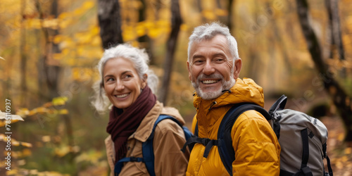 Joyful elderly couple with backpacks enjoying a hike among autumn leaves in the forest.