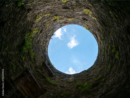 Stone well hole  old construction from inside  brick walls and blue sky background  fall down in the well concept