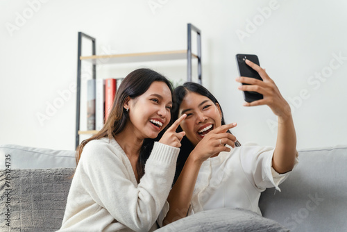 Two women are sitting on a couch and taking a selfie, look at the Smart phone, and laughing.