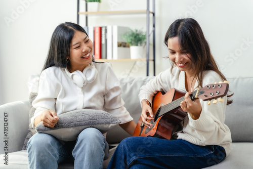 Two women are sitting on a couch, one of them playing a guitar