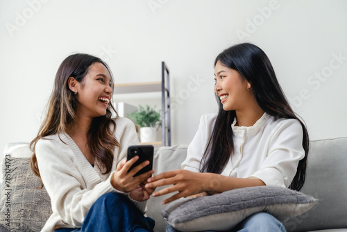 Two women sitting on a couch, one holding a cell phone, talking, smiling, and laughing.