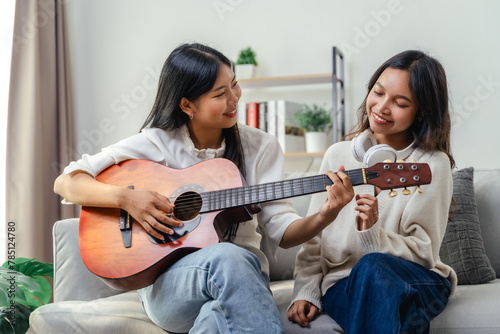 Two women are sitting on a couch, one of them playing a guitar