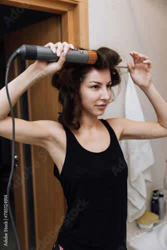 A girl dries her hair with a hairdryer in the bathroom in the morning