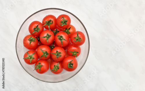 Cherry tomatoes in the glass bowl on the light gray marble table texture. Copy space. Top view.