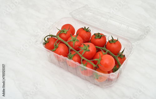 Cherry tomatoes in plastic retail supermarket packaging on the light gray marble table texture. Copy space.