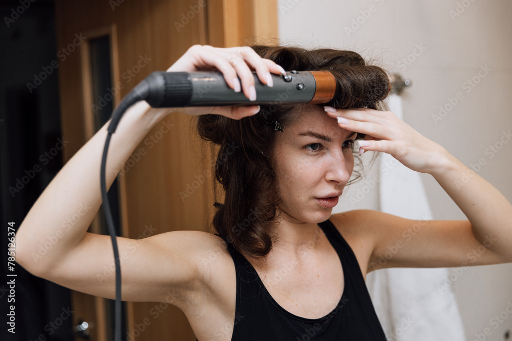 A girl dries her hair with a hairdryer in the bathroom in the morning