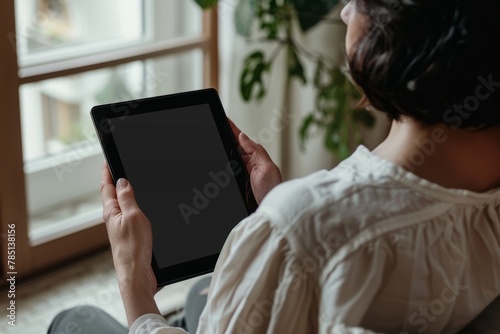 Display mockup from a shoulder angle of a mature woman holding an ebook with a completely black screen