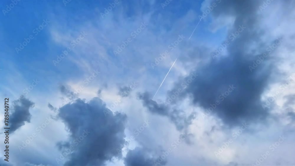 Low-angle shot of a cloud lapse with a contrail in the sky.