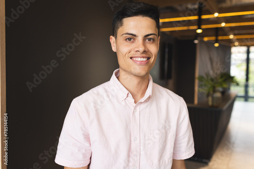 A young biracial man wearing a pink shirt is smiling in a modern business office