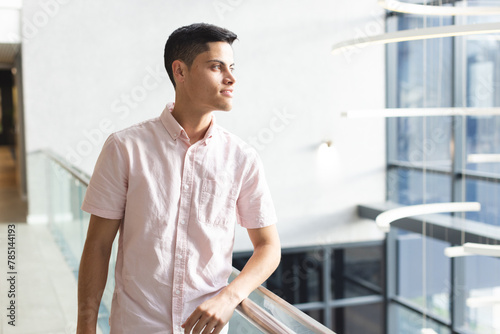 A young biracial man leaning on railing, looking to side in a modern business office with copy space