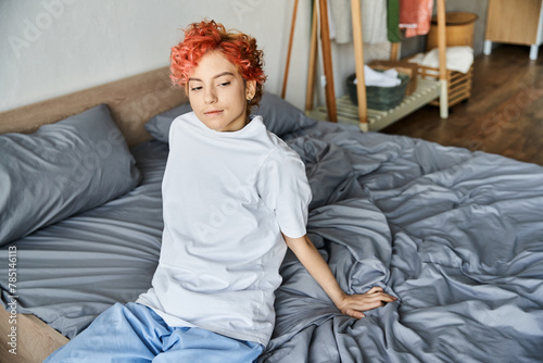 good looking extravagant person in white t shirt with red hair sitting on her bed, leisure time
