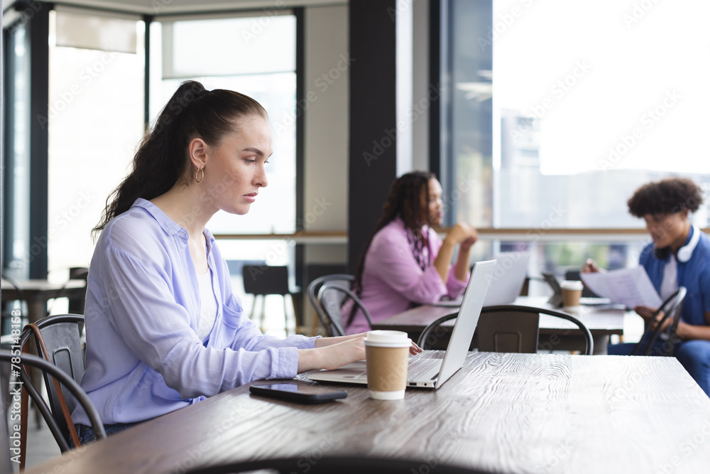 Caucasian woman typing on laptop in a modern business office, biracial woman and man talking Caucasian woman typing on laptop in a modern business office, biracial woman and man talking