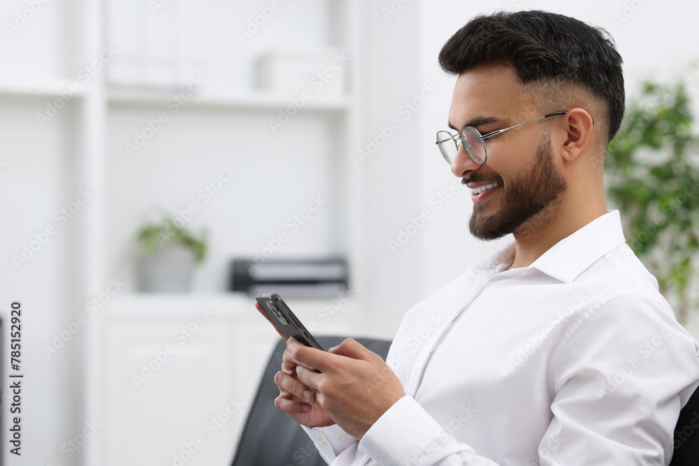 Happy young man using smartphone in office, space for text Happy young man using smartphone in office, space for text