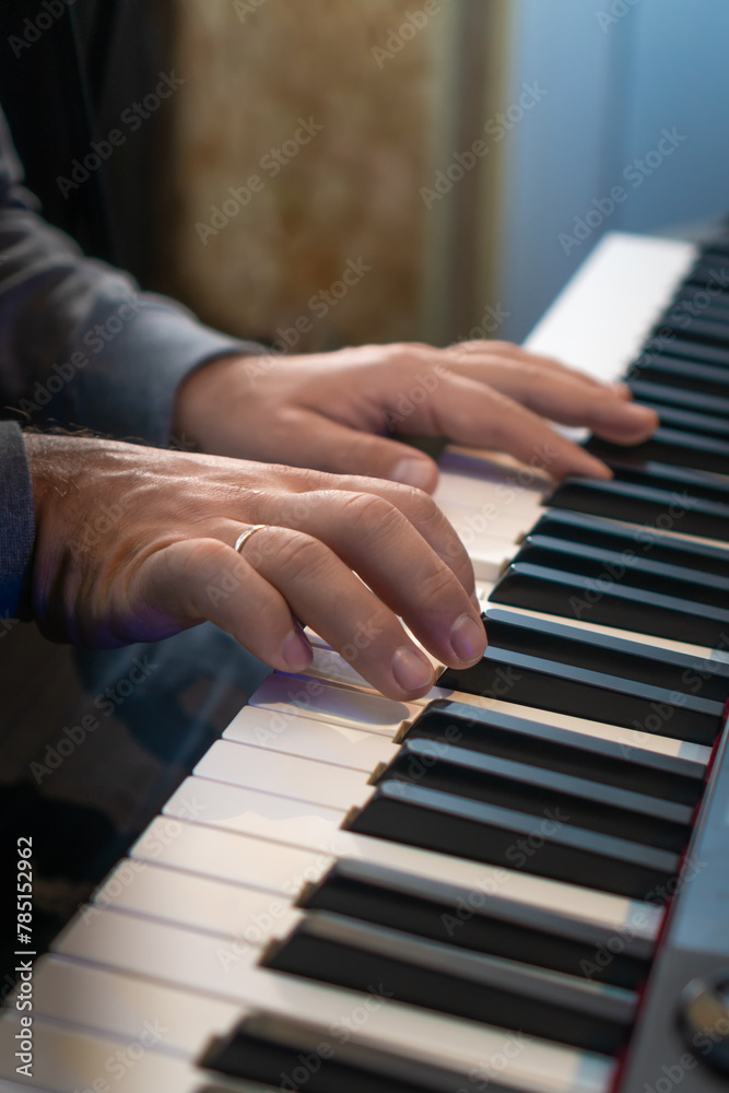 Close-up of male hands playing an electronic piano. Musical education at a music school. Private music lessons with a teacher. Vertical photo