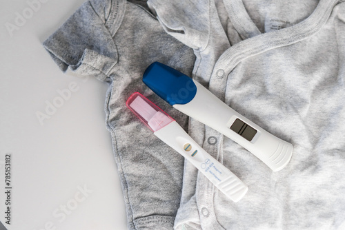 Top view of two positive pregnancy tests on baby clothes