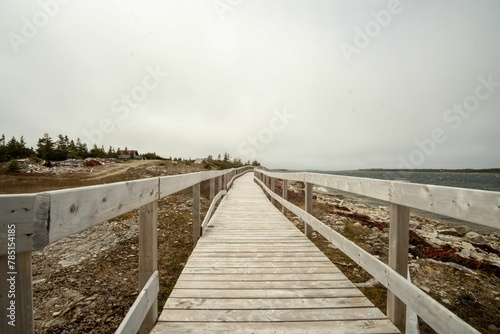 Long empty wooden walkway along the arid lakeshore under white sky © Wirestock