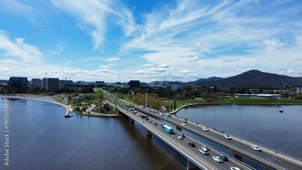 Bird's eye view of highways on bridges near a park and a lake under a blue cloudy sky