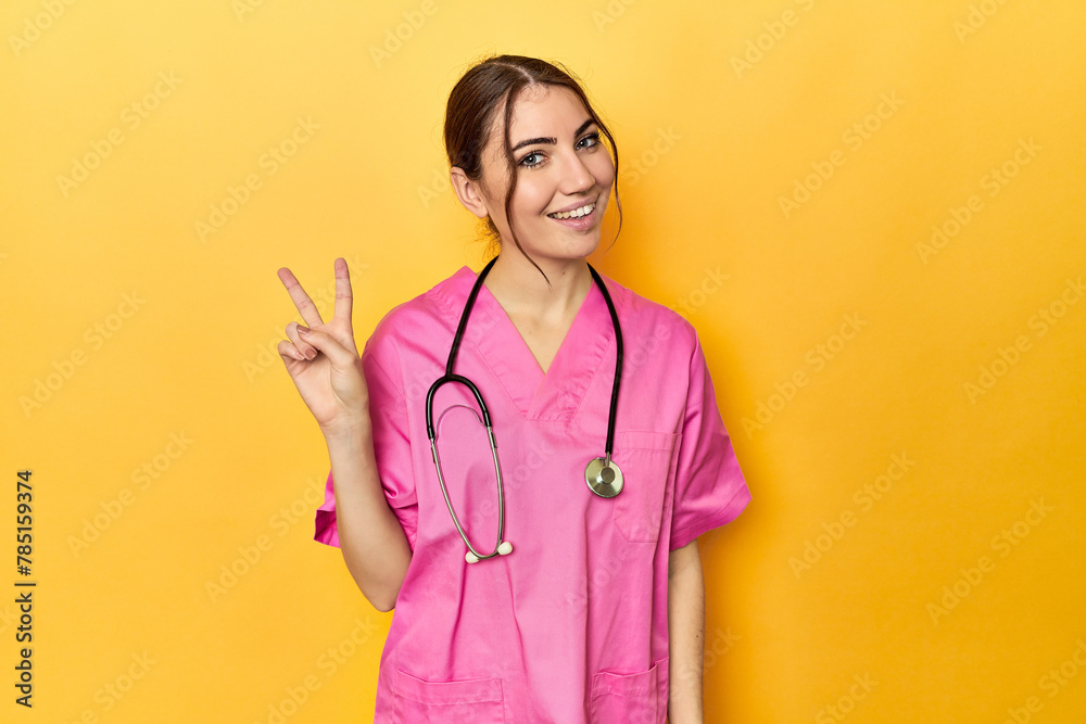 Nursing assistant in yellow background joyful and carefree showing a peace symbol with fingers. Nursing assistant in yellow background joyful and carefree showing a peace symbol with fingers.