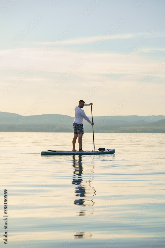 Joyful man is training SUP board on the lake. Stand up paddle boarding. Landscape in the background.