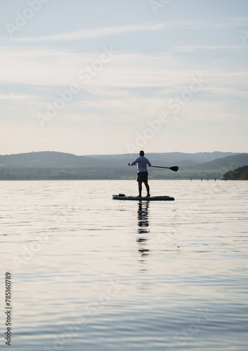 A man is training SUP board on the lake. Stand up paddle boarding. Landscape in the background. Enjoying the holiday. Active lifestyle. Silhouette of a man. Holding a paddle.