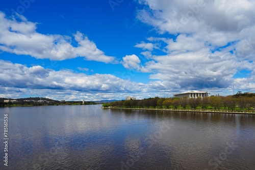 Fototapeta Naklejka Na Ścianę i Meble -  Scenic view of Lake Burley Griffin with row of trees on the shore under blue cloudy sky in Canberra