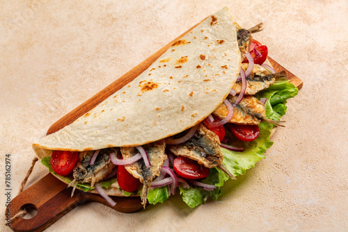 Traditional italian wrap or open sandwich. Piadina romagnola con sarde fritte. Fatbread with fried sardines fish, tomatoes, red onion and lettuce. Street food. photo