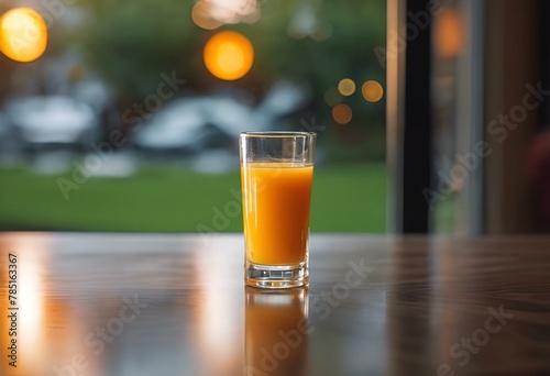 a glass of orange juice sitting on a wooden table in front of a window