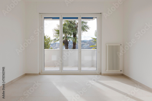 Empty space sconces an open sliding door in the background. On the ceiling there is a lighted LED and to the right a large window leading onto the balcony. It is a vuotom and modern  new flat. 