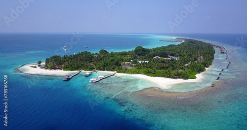 Aerial beautiful view of seascape in background of growing trees under blue bright sky in Maldives