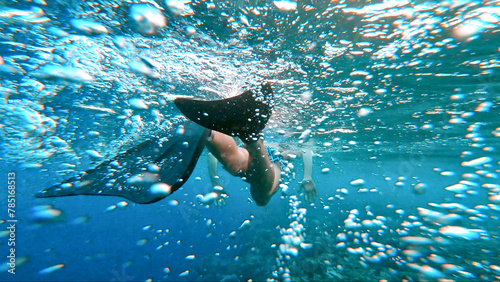 The men swim into the sea underwater. A close-up look from behind at the flippers. Bubbles under water formed from rapid movement of the legs.
