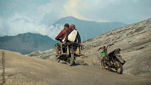 Two Indonesian people on a motorcycle ride through a volcanic desert photo