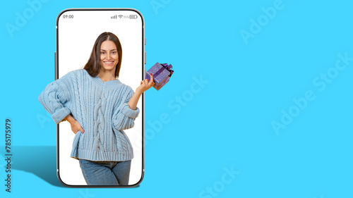 Woman with gift box in hands. Girl in screen of large phone. Promoter announces prize draw. Gift for woman birthday. Lady with gift on blue background. Concept of draw in mobile application