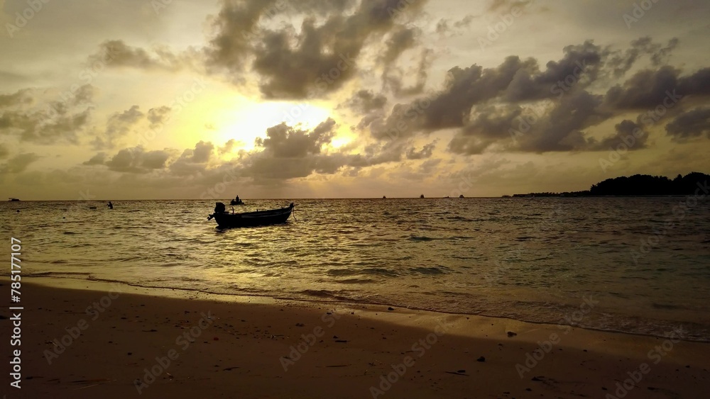 Silhouette of a small boat in the sea under a cloudy sky during sunset in the Maldives, Asia