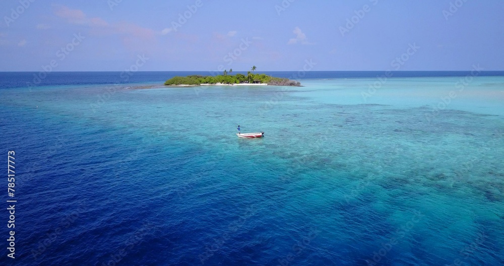 Aerial scenic view of turquoise water with coral reef and boat far from an island in the Maldives
