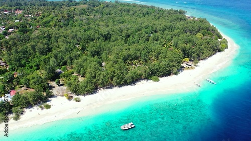 Aerial view of turquoise water with boats by a beach with trees in the Maldives