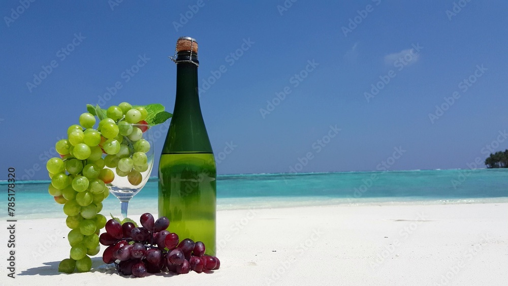 Closeup of a wine bottle with grapes at a beach on a sunny day