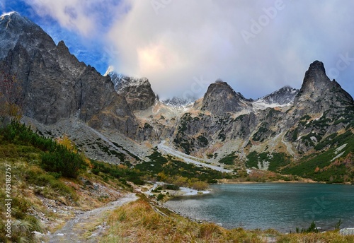 Fototapeta Naklejka Na Ścianę i Meble -  Panoramic photo of the rocky peaks of the High Tatras with the first layer of snow in early autumn above a clear turquoise glacial lake