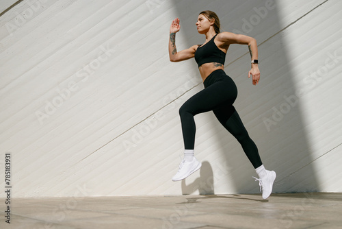 Fit woman athlete in sportswear is running on modern buildings background. Active lifestyle concept