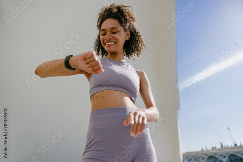 Smiling woman in sportswear looking on smartwatch after training. Outdoor sports in the morning