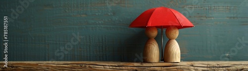 Wooden man and woman figures, sheltered by red umbrella, family protection theme, room for text