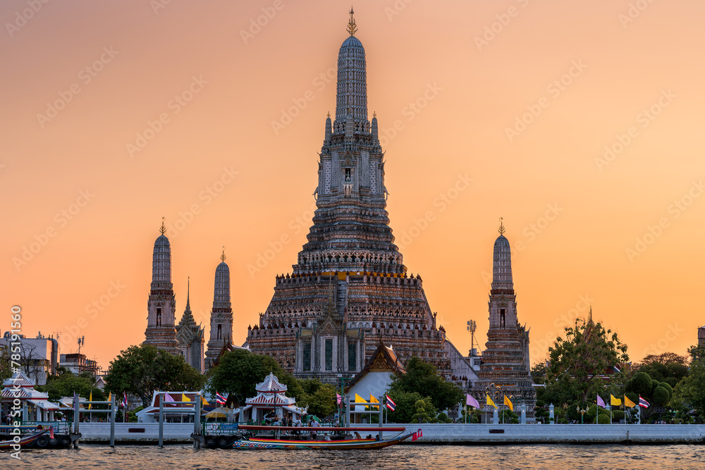 Fototapeta premium Wat Arun stupa, a significant landmark of Bangkok, Thailand, stands prominently along the Chao Phraya River, with a beautiful sunset sky.