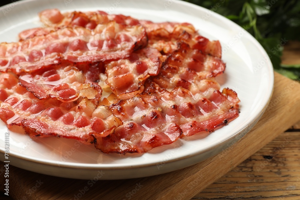 Plate with fried bacon slices on wooden table, closeup