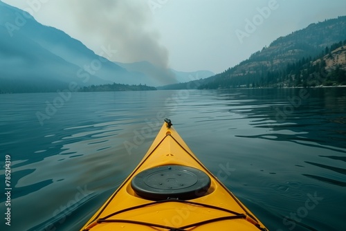 A closeup shot of the front tip of an open yellow kayak on calm waters, with mountains in misty background, smoke from forest fires creating hazy atmosphere, stunning natural color