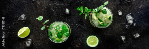 Mojito cocktail overhead flat lay panorama. Summer cold drink with lime, fresh mint, and ice. Cool beverage on a black background © laplateresca