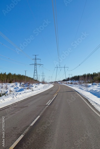 High-voltage power lines and road in sunny winter weather with snow on the ground, Loviisa, Finland.