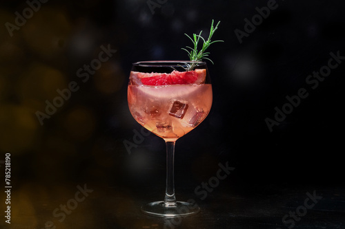 Fancy cocktail with fresh fruit. Gin and tonic drink with ice at a party, on a black background. Alcohol with pink grapefuit and rosemary, toned image