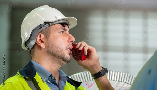 male maintenance engineer in uniform helmet safety talk by walki talkie and inspection check control heavy machine in industrial factory. technician worker use radio check for repair factory machine photo