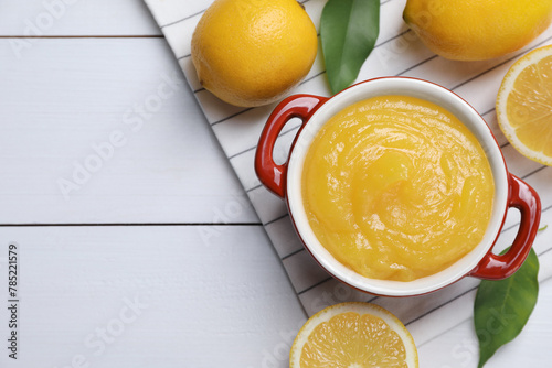 Delicious lemon curd in bowl and fresh citrus fruits on white wooden table, flat lay. Space for text