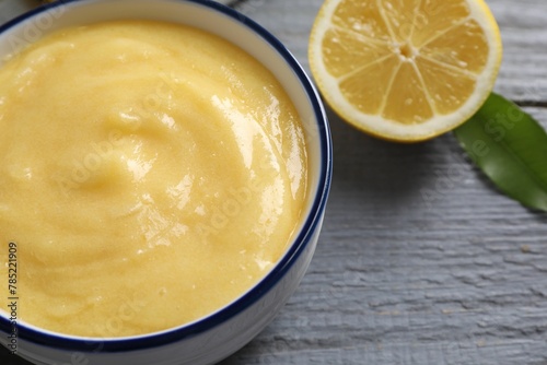 Delicious lemon curd in bowl  fresh citrus fruit and green leaf on grey wooden table  closeup